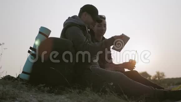 日落时一对年轻的游客坐在山顶上享受一块石碑视频的预览图