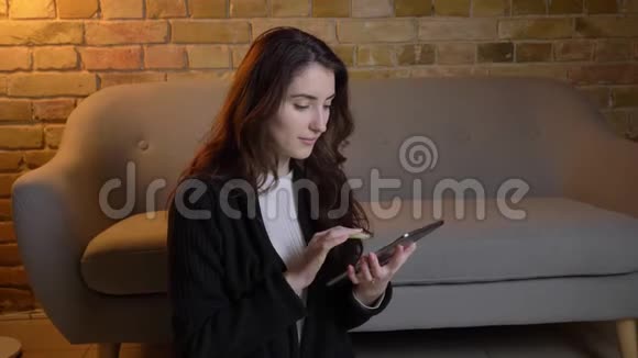 年轻的白种人女孩波浪状的头发坐在地板上在舒适的家庭氛围中愉快地展示着绿色的平板电脑屏幕视频的预览图