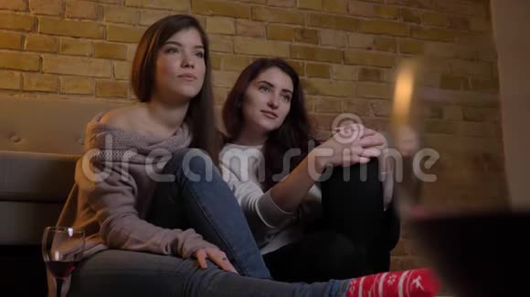 快乐的年轻白种人女性朋友在舒适的家庭背景下看电视和交谈的肖像视频的预览图