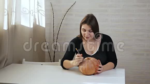 万圣节的概念快乐的女孩坐在一张桌子上南瓜在万圣节南瓜上画眼睛和嘴巴视频的预览图