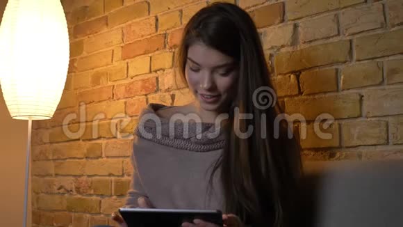 年轻的白种人女孩坐在沙发上观看平板电脑的肖像充满创造力和对舒适的家的兴趣视频的预览图