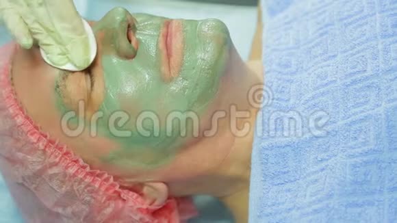 一位女性美容师用棉垫从一个男人的脸上取出一个治疗泥面膜侧视图视频的预览图