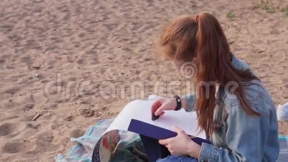 女孩坐在海滩上在海上画夏天的日落视频的预览图