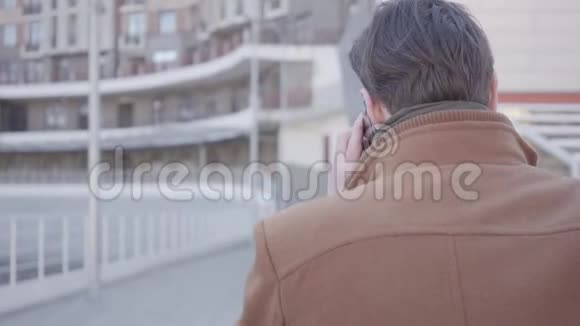 棕色外套的英俊自信男子走在城市街道上用手机交谈的背景城市景观视频的预览图