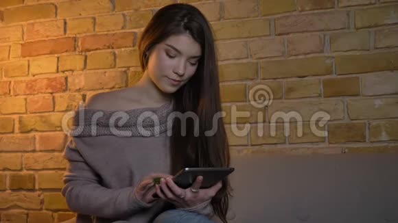 一张年轻的白人女孩的特写照片在舒适的家庭背景下愉快地将平板电脑的绿色屏幕放进相机视频的预览图