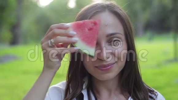 特写女孩的肖像闻着香气吃着一个红色的健康多汁的西瓜在绿色的西瓜上傻笑视频的预览图