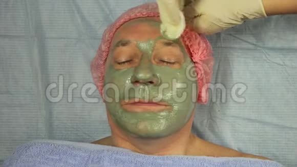 美容师的手用棉垫从男人脸上取下一个泥面膜视频的预览图