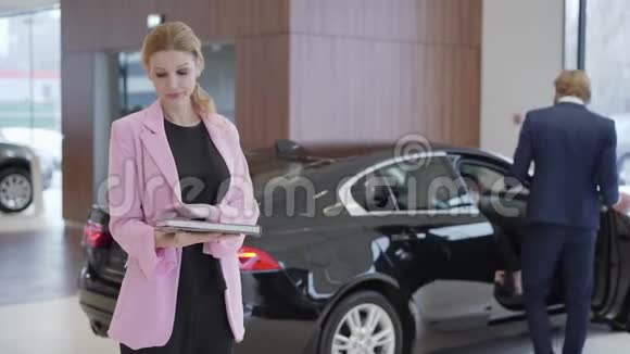 一幅可爱的可爱女孩穿着粉红色夹克的肖像在夫妇选择车辆之前有一本关于汽车的大书打开门视频的预览图