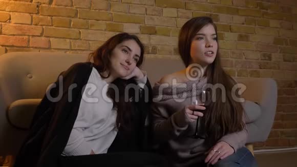 在舒适的家庭背景下年轻的白种人女孩兴高采烈地看着电视喝着葡萄酒的特写肖像视频的预览图