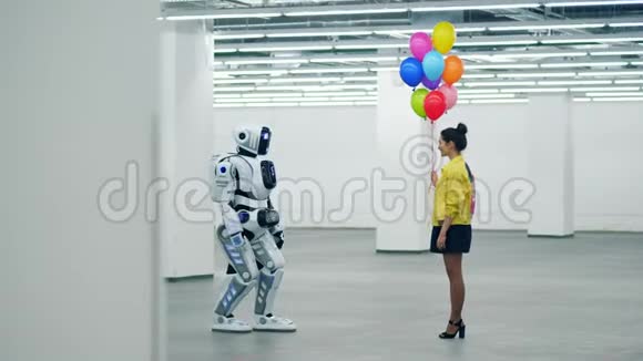 一个女孩正在空厅里给一个机器人送气球视频的预览图