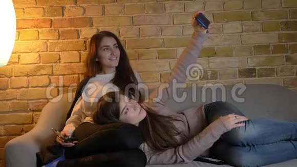 年轻的高加索女孩在沙发上放松在舒适的家庭氛围中使用智能手机制作自拍照片的肖像视频的预览图