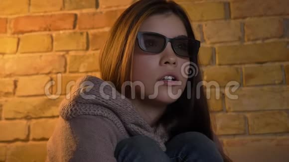 一位戴着3D眼镜的年轻白种人女孩的特写肖像她在沙发上靠着电视观看恐怖电影害怕舒适视频的预览图