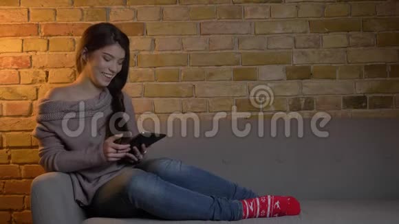 年轻的白种人女孩坐在沙发上看着平板电脑在舒适的家里把绿色的屏幕显示成相机视频的预览图