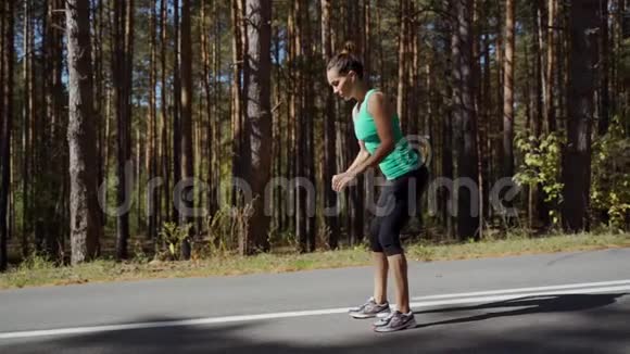 女孩蹲在森林里的沥青路上美丽的卷发运动女孩在夏日户外健身视频的预览图