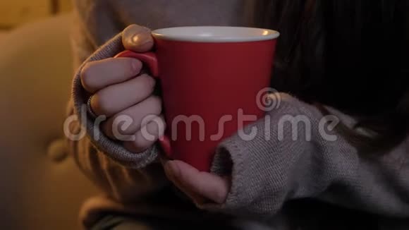 在舒适的家庭背景上用热饮料特写女性手拿红色杯子的肖像视频的预览图
