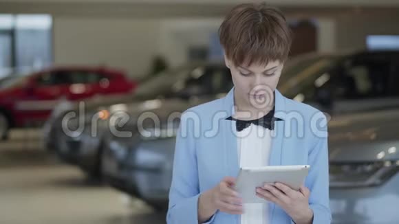 肖像自信可爱的女人在正式穿着她的平板电脑站在模糊的汽车前面在车展上视频的预览图