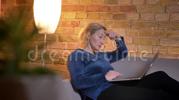 在笔记本电脑上工作坐在室内沙发上体贴入微的白种人女性特写镜头视频的预览图