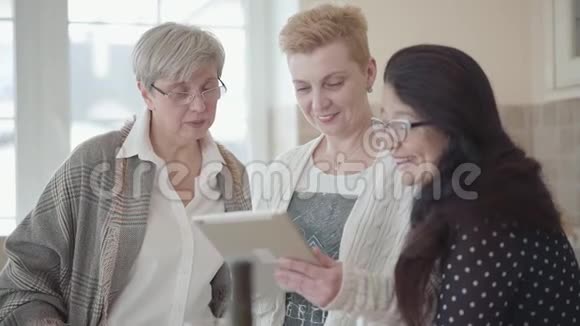成年女性的肖像在平板电脑上向她的朋友展示照片微笑着三名中年妇女进行交流视频的预览图