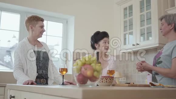 成年快乐的女朋友笑着在餐桌上和厨房里的水果和葡萄酒聊天长者视频的预览图