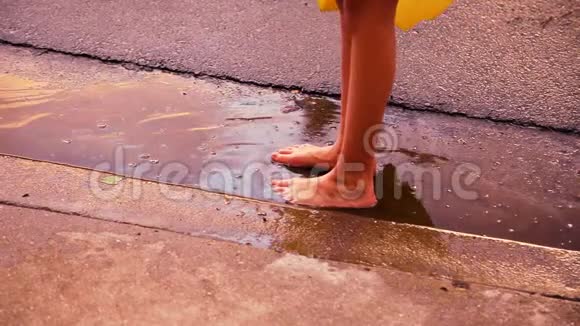 一个孩子赤脚站在车道底部的水坑里他们动作缓慢溅起水花降落视频的预览图
