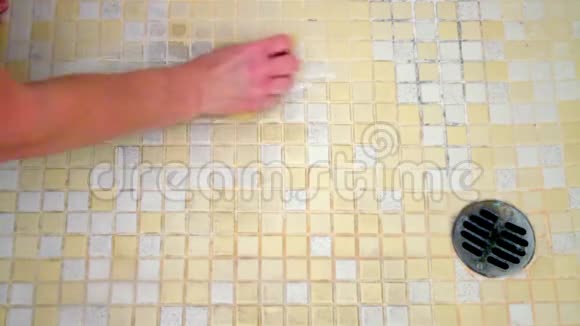 一个女人的手开始用海绵清洁由黄色和白色瓷砖组成的肮脏的淋浴地板视频的预览图