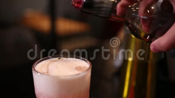 酒保将红色糖浆倒入带有冰块的刻有玻璃的粉红色鸡尾酒中视频的预览图