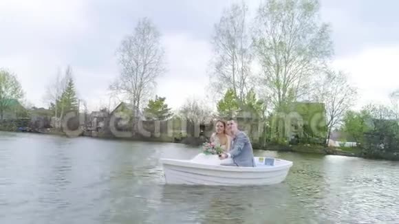 镜头移离坐在白色小船上快乐欢笑的新婚夫妇视频的预览图