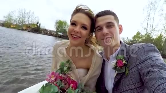 新婚夫妇坐在池塘边的小船上做着明亮的自拍快关门视频的预览图