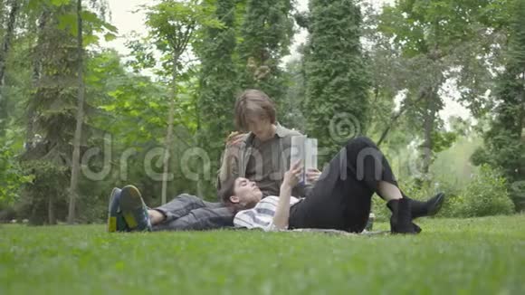 描绘一对穿着休闲服装的年轻夫妇在户外聚会约会坐在毯子上的家伙视频的预览图