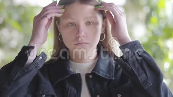 悲伤的少女在镜头中靠近她的头发的肖像年轻女子的手指穿过头发视频的预览图