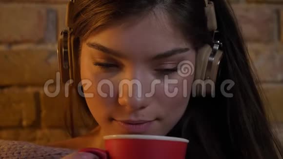 特写照片年轻的白种人女孩戴着耳机红色的杯子享受着布里肯墙背景上的饮料视频的预览图