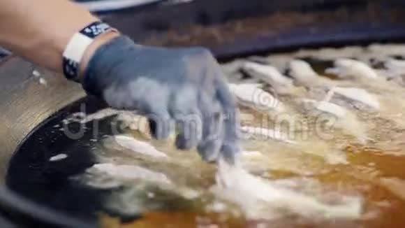 厨师把鱼放入热油中的戴手套的手视频的预览图