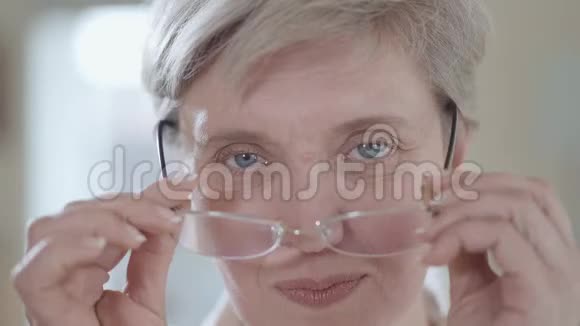 一个成熟的白发女人戴着眼镜近距离看着相机的肖像视频的预览图