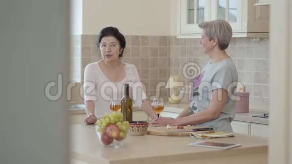 两个成熟的女人站在厨房的现代餐桌旁交流有感情地讲故事视频的预览图