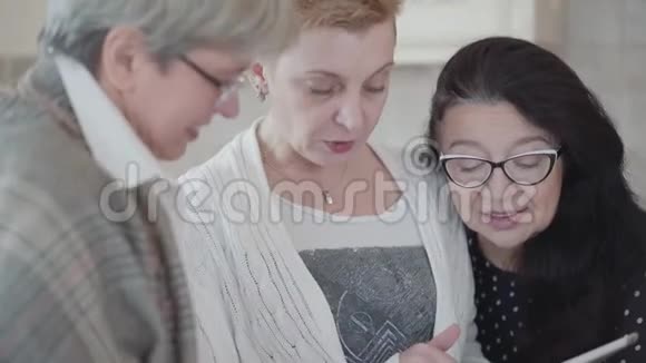 女士在平板电脑上向她的朋友展示照片三位中年妇女的小组交流视频的预览图