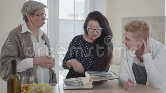 一位留着长发的老年妇女向朋友们展示她的旧相册三个中年成熟妇女组视频的预览图