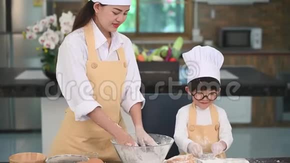 漂亮的女人和可爱的亚洲小男孩戴着眼镜戴着厨师帽围着围裙在家里的厨房里玩耍和烤面包霍姆视频的预览图