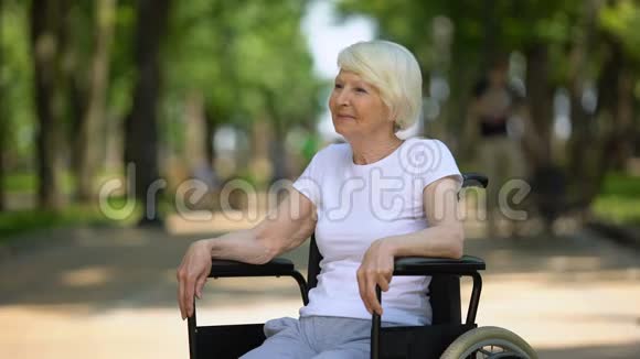 坐在轮椅上微笑的老妇人在医院公园享受阳光明媚的一天康复了视频的预览图