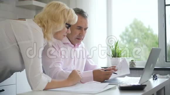 男人和女人说话在家庭房间的桌子上看监视器视频的预览图