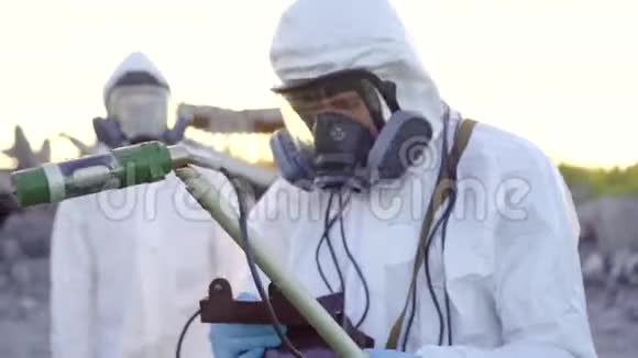 两名穿着白色工作服和防护面罩的科学家在日落时测量辐射的肖像视频的预览图
