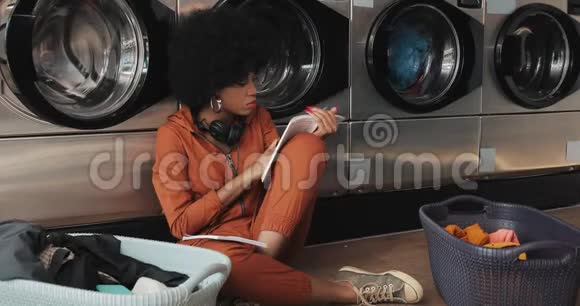 漂亮的非洲裔美国年轻女性在洗衣店洗衣服时看书和写纸条视频的预览图
