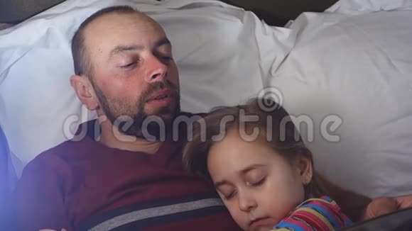 父亲给女儿读睡前故事女儿睡在她父亲身边父亲读她的书视频的预览图