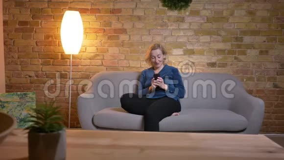 在舒适的沙发上坐着时用电话微笑着放松的老白种人女性的特写照片视频的预览图
