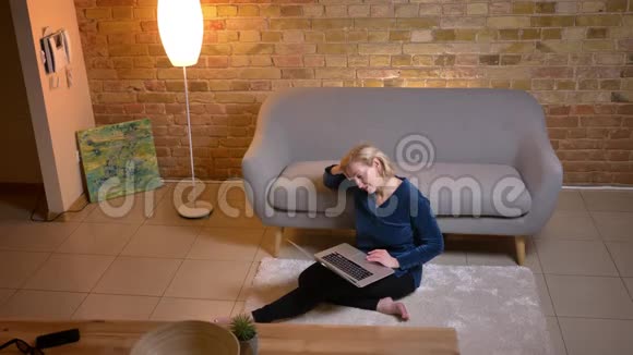 白种人年长女性在坐在地板上休息时用笔记本电脑观看节目的特写镜头视频的预览图