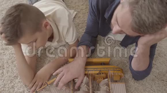 肖像可爱的父亲和他的儿子躺在地上毛茸茸的地毯上玩船模特写镜头视频的预览图