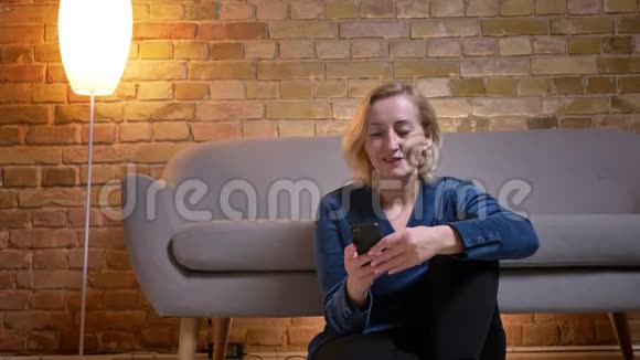 一个舒适的公寓里坐在地板上时一位年长的白种人女用手机发短信的特写镜头视频的预览图