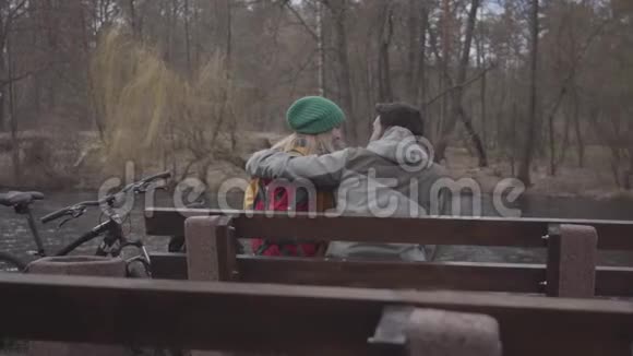 在河岸的春天公园里年轻夫妇背着背包坐在长凳上有胡子的视频的预览图