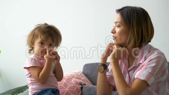幸福美丽有爱的家庭年轻的母亲和女儿坐在沙发上笑着鬼鬼祟祟地走来走去视频的预览图