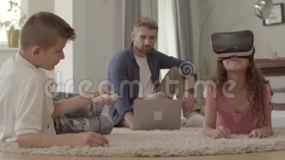 兄妹俩用虚拟现实眼镜躺在松软的地毯上父亲坐在地上视频的预览图