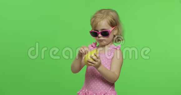 穿着粉红色泳衣和太阳镜的孩子吃一个绿色的梨色度键视频的预览图